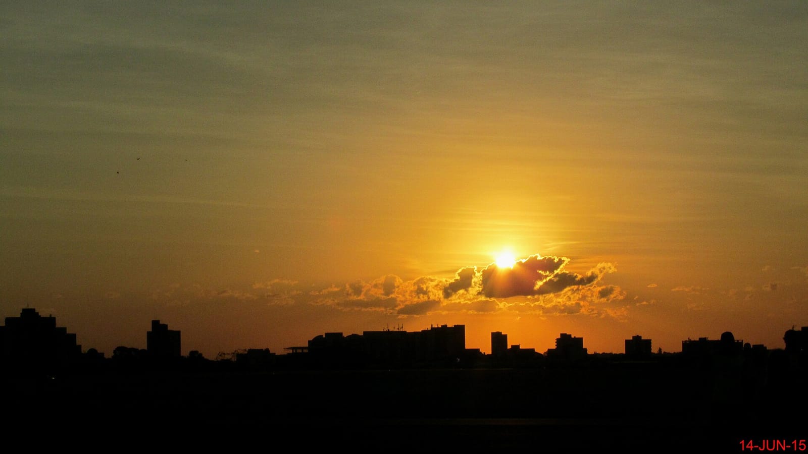 Céu com sol entre nuvens sobre área urbana em manhã fria